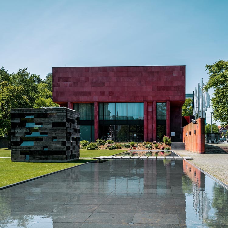 Kunsthalle Bielefeld mit dem markanten roten Baukörper und dem angrenzenden Skulpturenpark bei Sonnenschein.