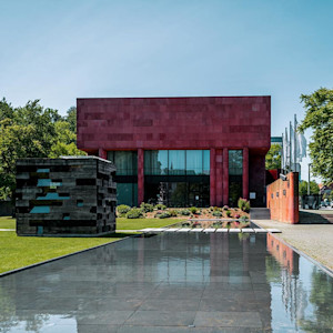 Kunsthalle Bielefeld mit dem markanten roten Baukörper und dem angrenzenden Skulpturenpark bei Sonnenschein.
