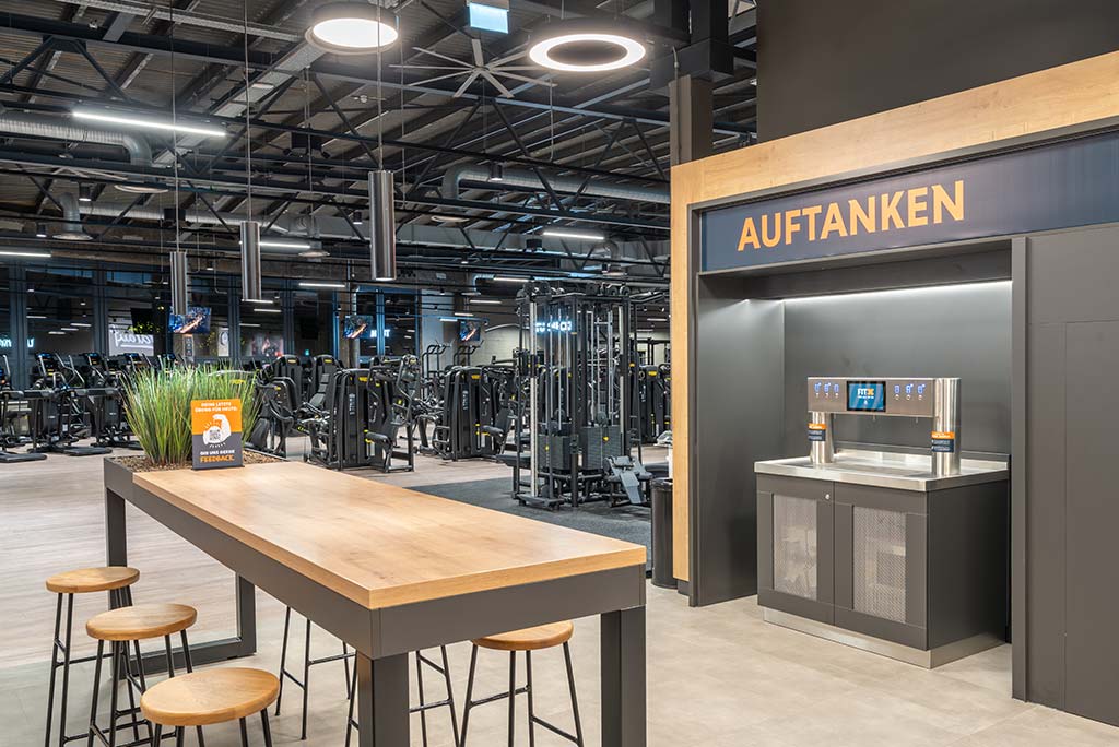 Abgetrennter Lounge-Bereich im FitX Fitnessstudio Berlin-Ku'damm mit verschiedenen Sitzmöglichkeiten. Der Bereich ist hell, freundlich und im industriellen Design gestaltet.