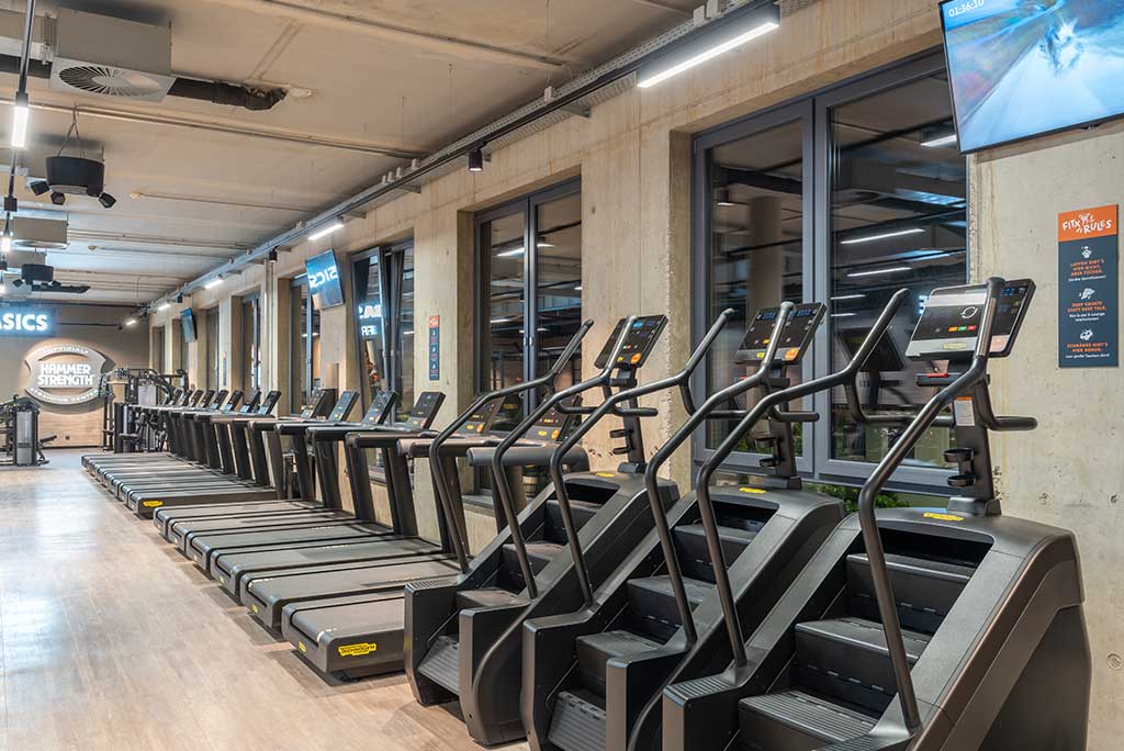 Offener Bereich für Ausdauertraining im FitX Fitnessstudio Troisdorf-Mitte mit verschiedenen Cardio-Geräten. An den Wänden hängen Fernseher.