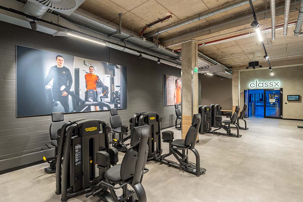 Gerätebereich im FitX Fitnessstudio Essen-Bergerhausen mit verschiedenen Kraftgeräten. Der Raum ist im industriellen Design gestaltet, mit offenen Deckenstrukturen und hellen Böden.