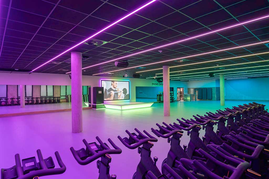 Großer, offener Kursraum im FitX Fitnessstudio Troisdorf-Mitte. An der hinteren Wand befindet sich eine erhöhte Bühne, dahinter eine Leinwand. Links und rechts davon sind Spiegelwände.