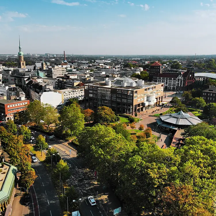 Luftaufnahme der Dortmunder Innenstadt mit dem Friedensplatz, umgeben von modernen und historischen Gebäuden, sowie viel Grün.