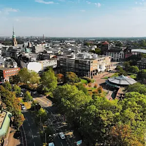 Luftaufnahme der Dortmunder Innenstadt mit dem Friedensplatz, umgeben von modernen und historischen Gebäuden, sowie viel Grün.