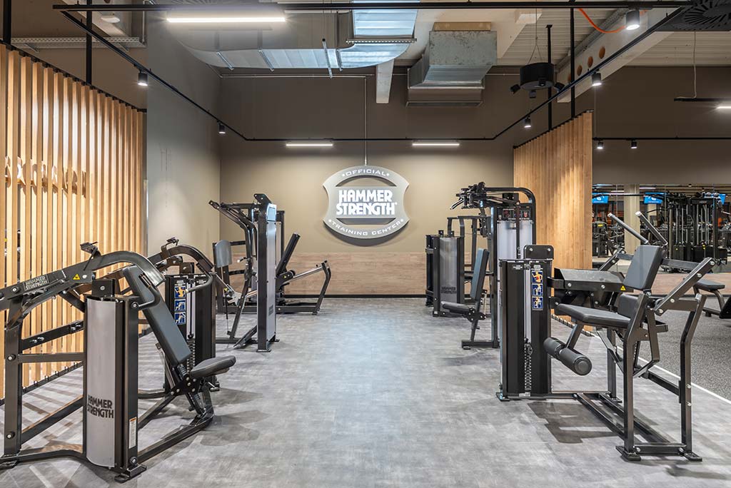 Zirkel-Bereich im FitX Fitnessstudio Augsburg-Lechhausen, in dem verschiedene Trainingsgeräte kreisförmig angeordnet sind. Über den Geräten hängt ein großer Leuchtring, der in grün oder rot leuchtet und die Übungsdauer anzeigt.