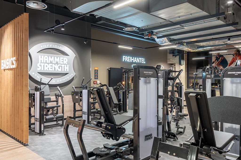 Zirkel-Bereich im FitX Fitnessstudio Berlin-Ku'damm, in dem verschiedene Trainingsgeräte kreisförmig angeordnet sind. Über den Geräten hängt ein großer Leuchtring, der in grün oder rot leuchtet und die Übungsdauer anzeigt.