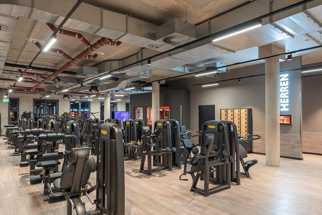 Gerätebereich im FitX Fitnessstudio Troisdorf-Mitte mit verschiedenen Kraftgeräten. Der Raum ist im industriellen Design gestaltet, mit offenen Deckenstrukturen und hellen Böden.
