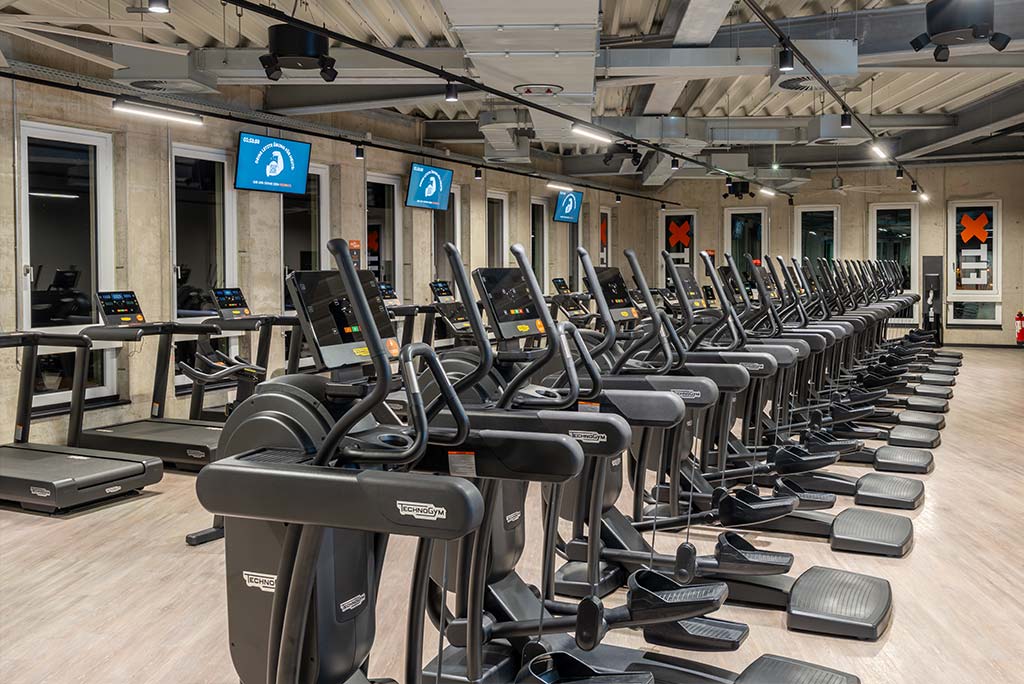 Offener Bereich für Ausdauertraining im FitX Fitnessstudio Mülheim-Stadtmitte mit verschiedenen Cardio-Geräten. An den Wänden hängen Fernseher.