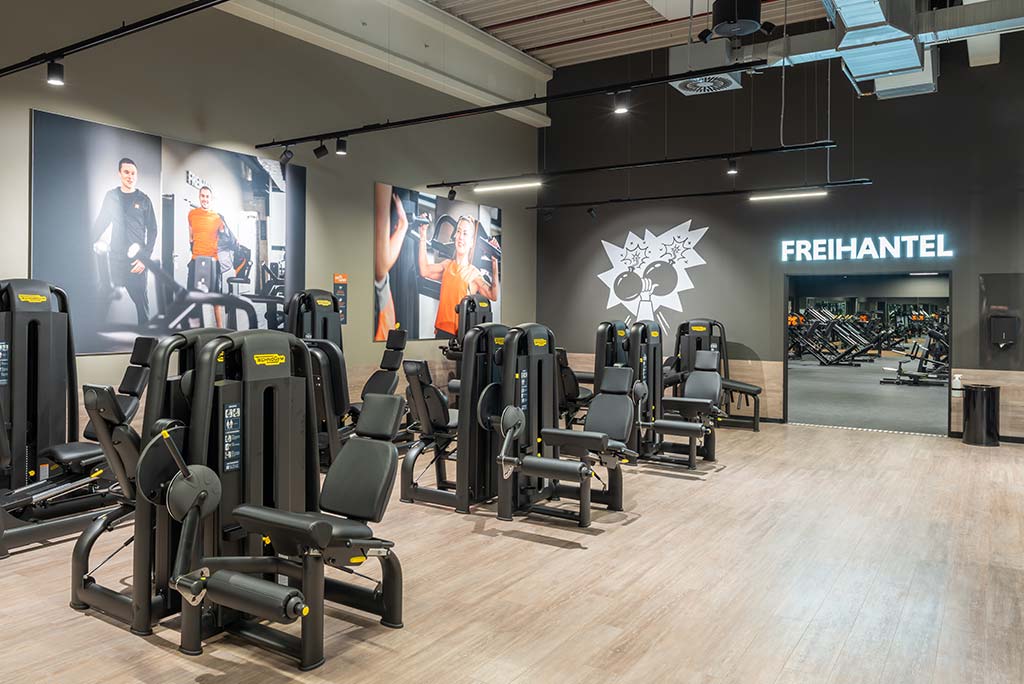 Gerätebereich im FitX Fitnessstudio Dortmund-Phoenix See mit verschiedenen Kraftgeräten. Der Raum ist im industriellen Design gestaltet, mit offenen Deckenstrukturen und hellen Böden.