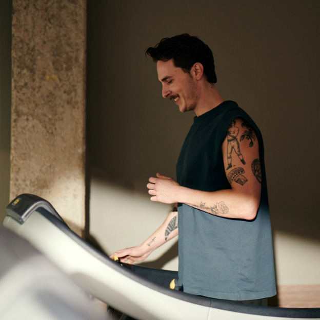 Bild: Ein junger Mann läuft im Cardiobereich auf einem Laufband und schaut dabei lächelnd auf das Display des Laufbandes.
