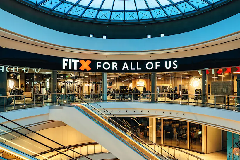 Bild: Außenansicht eines FitX Fitnessstudios. Ein großes FitX-Logo mit orangefarbenem X ist zu sehen. Das Gebäude befindet sich in einem urbanen Umfeld.