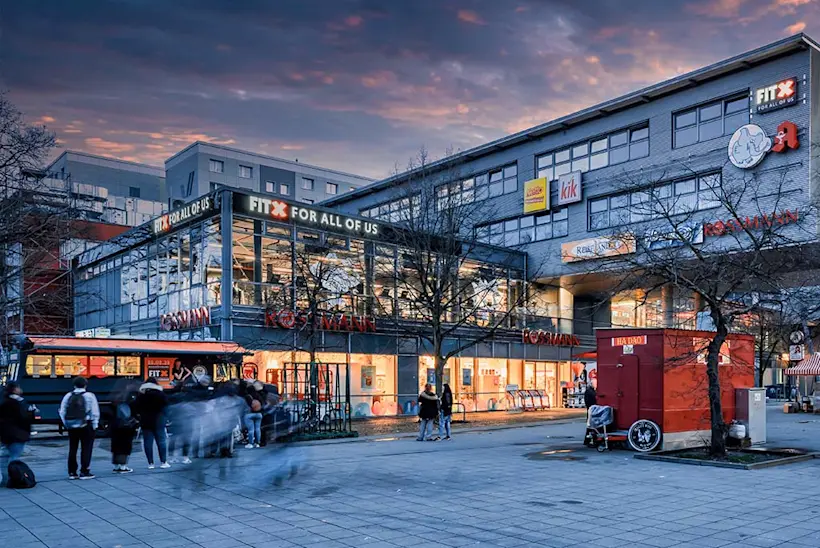 Bild: Außenansicht eines FitX Fitnessstudios. Ein großes FitX-Logo mit orangefarbenem X ist zu sehen. Das Gebäude befindet sich in einem urbanen Umfeld.