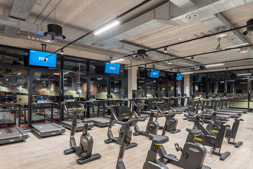 Offener Bereich für Ausdauertraining im FitX Fitnessstudio Remscheid-Süd mit verschiedenen Cardio-Geräten. An den Wänden hängen Fernseher.