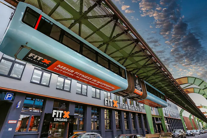 Bild: Außenansicht eines FitX Fitnessstudios. Ein großes FitX-Logo mit orangefarbenem X ist zu sehen. Das Gebäude befindet sich in einem urbanen Umfeld.