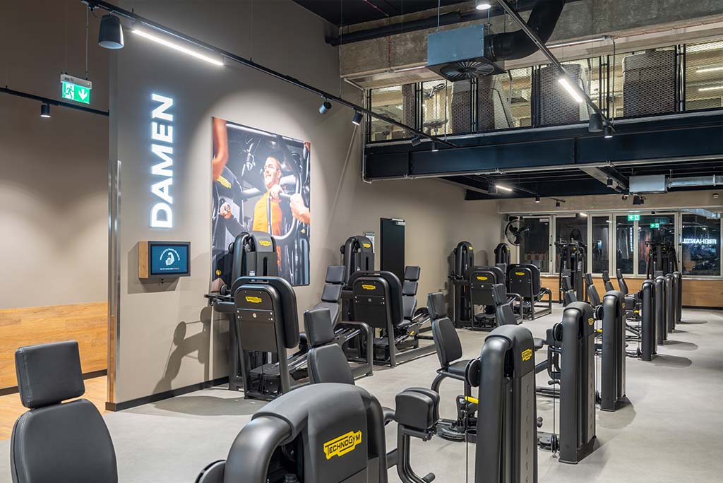 Gerätebereich im FitX Fitnessstudio Düsseldorf-Derendorf mit verschiedenen Kraftgeräten. Der Raum ist im industriellen Design gestaltet, mit offenen Deckenstrukturen und hellen Böden.