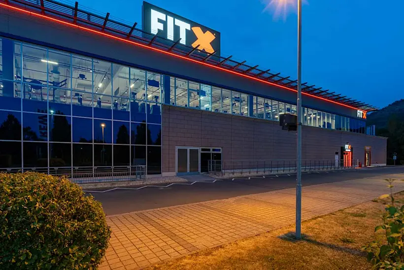 Bild: Außenansicht eines FitX Fitnessstudios. Ein großes FitX-Logo mit orangefarbenem X ist zu sehen. Das Gebäude befindet sich in einem urbanen Umfeld.