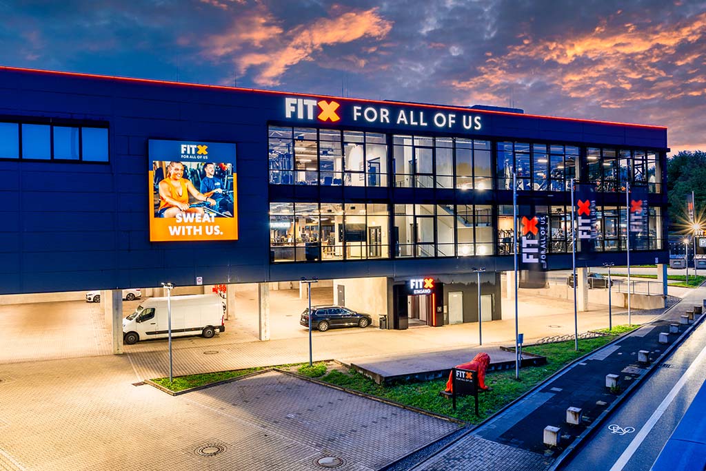 Außenansicht des FitX Fitnessstudios Remscheid-Süd. Ein großes FitX-Logo mit orangefarbenem X ist zu sehen. Das Gebäude befindet sich in einem urbanen Umfeld.