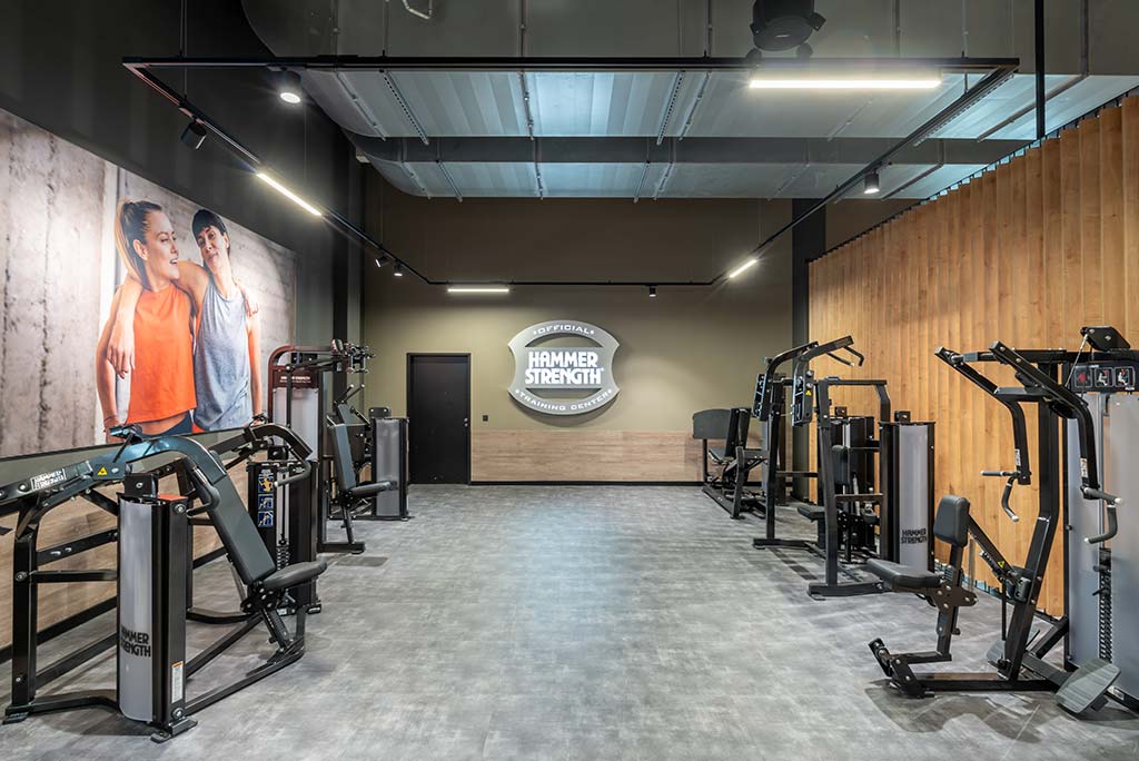 Zirkel-Bereich im FitX Fitnessstudio Dortmund-Phoenix See, in dem verschiedene Trainingsgeräte kreisförmig angeordnet sind. Über den Geräten hängt ein großer Leuchtring, der in grün oder rot leuchtet und die Übungsdauer anzeigt.