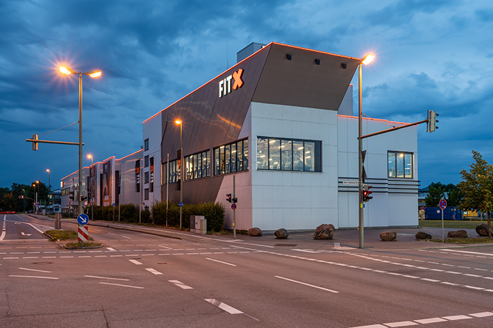 Außenansicht des FitX Fitnessstudios Augsburg-Lechhausen. Ein großes FitX-Logo mit orangefarbenem X ist zu sehen. Das Gebäude befindet sich in einem urbanen Umfeld.