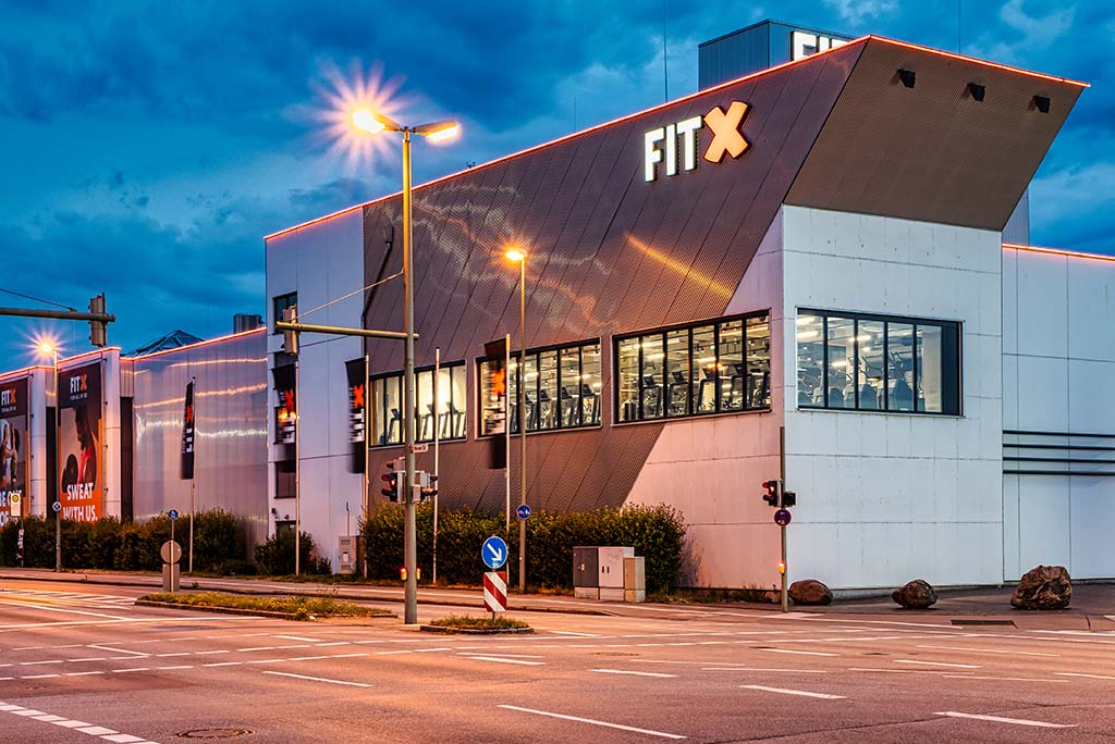 Außenansicht des FitX Fitnessstudios Augsburg-Lechhausen. Ein großes FitX-Logo mit orangefarbenem X ist zu sehen. Das Gebäude befindet sich in einem urbanen Umfeld.