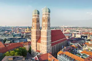 Panoramaaufnahme von München bei Tag mit Blick auf die Frauenkirche, die Zwiebelkuppeln und die Dächer der Altstadt.