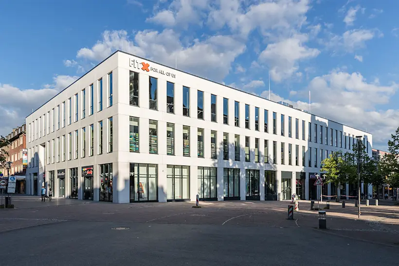 Bild: Außenansicht eines FitX Fitnessstudios. Ein großes FitX-Logo mit orangefarbenem X ist zu sehen. Das Gebäude befindet sich in einem urbanen Umfeld.