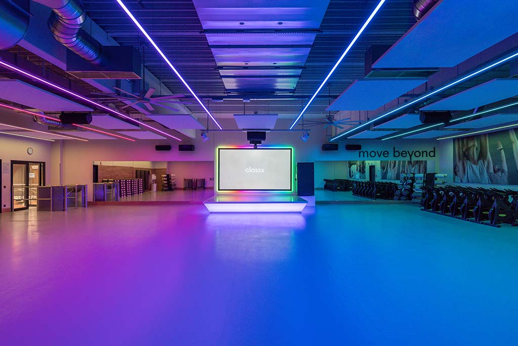 Großer, offener Kursraum im FitX Fitnessstudio Wuppertal-Elberfeld. An der hinteren Wand befindet sich eine erhöhte Bühne, dahinter eine Leinwand. Links und rechts davon sind Spiegelwände.