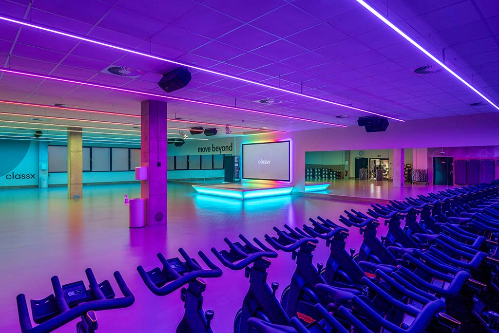Großer, offener Kursraum im FitX Fitnessstudio Remscheid-Süd. An der hinteren Wand befindet sich eine erhöhte Bühne, dahinter eine Leinwand. Links und rechts davon sind Spiegelwände.