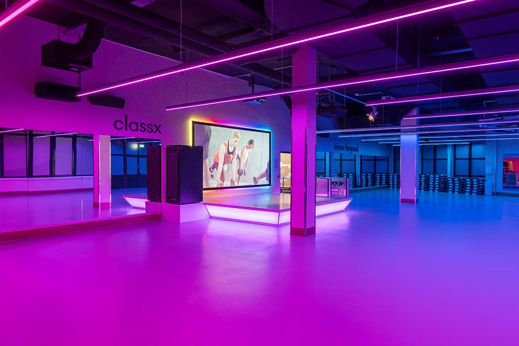Großer, offener Kursraum im FitX Fitnessstudio Düsseldorf-Derendorf. An der hinteren Wand befindet sich eine erhöhte Bühne, dahinter eine Leinwand. Links und rechts davon sind Spiegelwände.