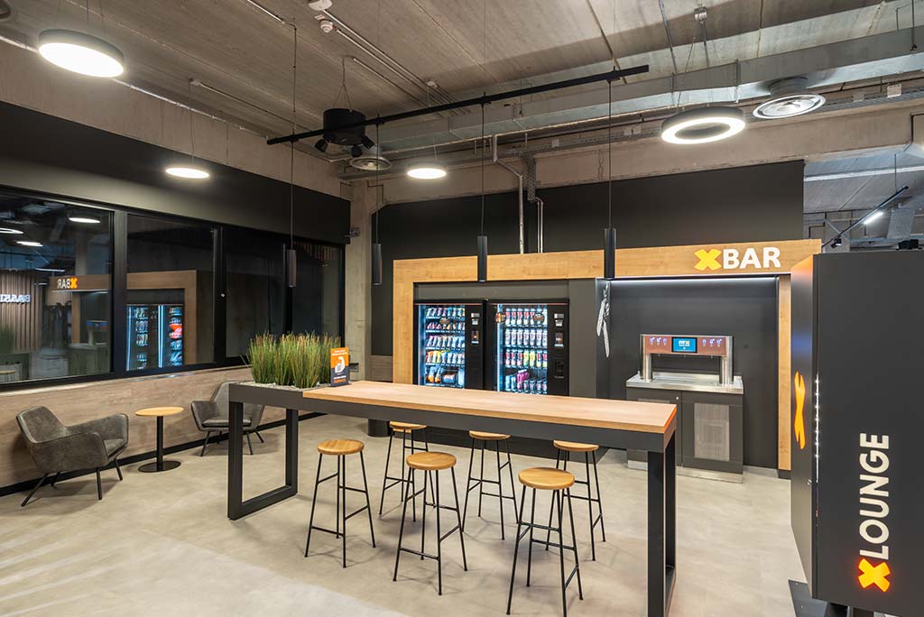 Abgetrennter Lounge-Bereich im FitX Fitnessstudio Remscheid-Süd mit verschiedenen Sitzmöglichkeiten. Der Bereich ist hell, freundlich und im industriellen Design gestaltet.