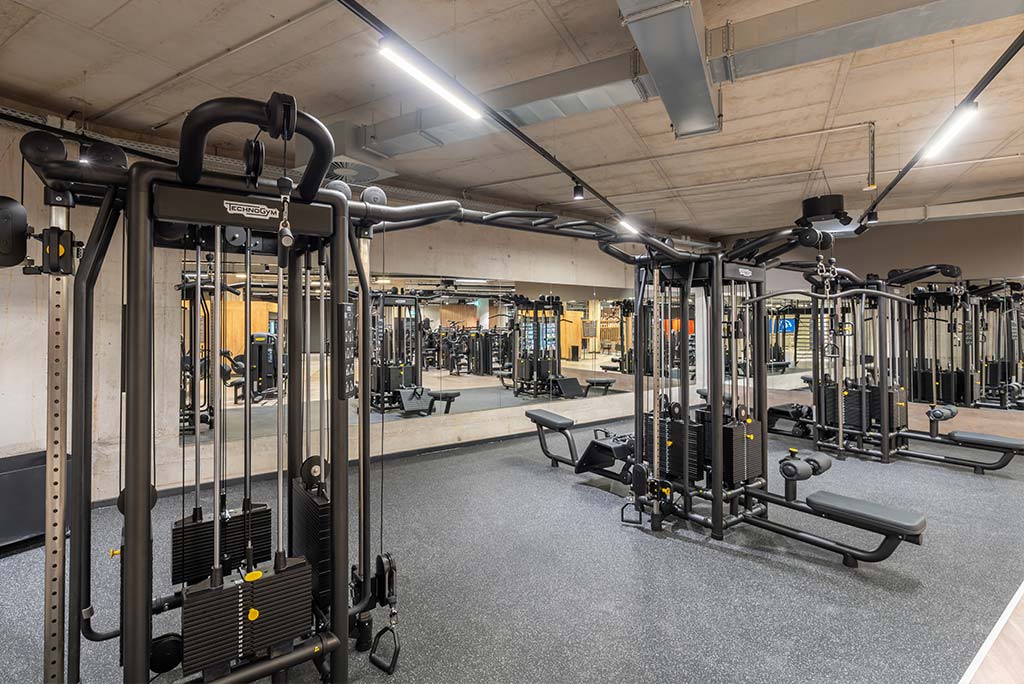 Gerätebereich im FitX Fitnessstudio Mülheim-Stadtmitte mit verschiedenen Kraftgeräten. Der Raum ist im industriellen Design gestaltet, mit offenen Deckenstrukturen und hellen Böden.