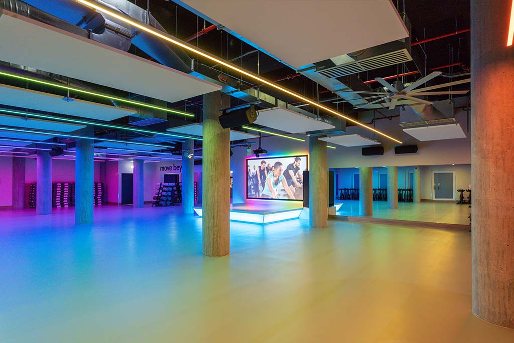 Großer, offener Kursraum im FitX Fitnessstudio Böblingen-Zentrum. An der hinteren Wand befindet sich eine erhöhte Bühne, dahinter eine Leinwand. Links und rechts davon sind Spiegelwände.