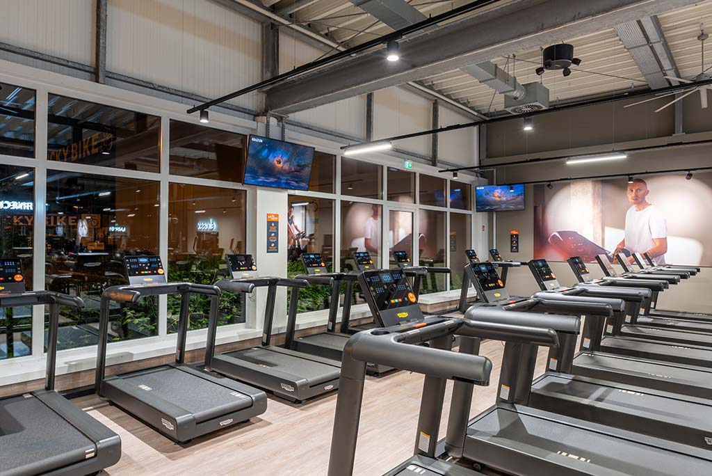 Offener Bereich für Ausdauertraining im FitX Fitnessstudio Dortmund-Phoenix See mit verschiedenen Cardio-Geräten. An den Wänden hängen Fernseher.