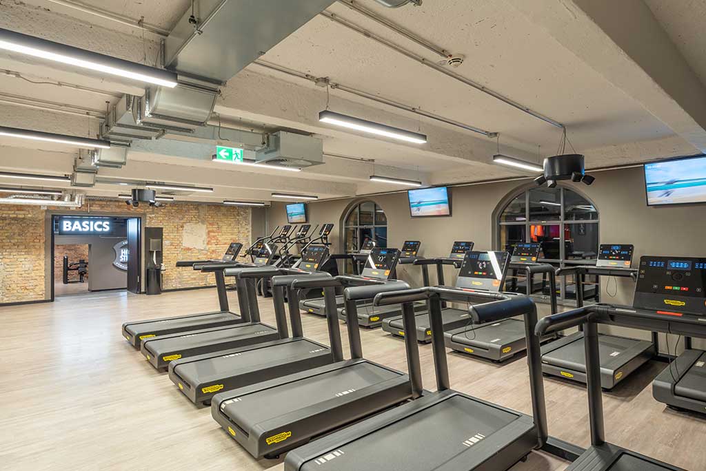 Offener Bereich für Ausdauertraining im FitX Fitnessstudio Berlin-Moabit mit verschiedenen Cardio-Geräten. An den Wänden hängen Fernseher.