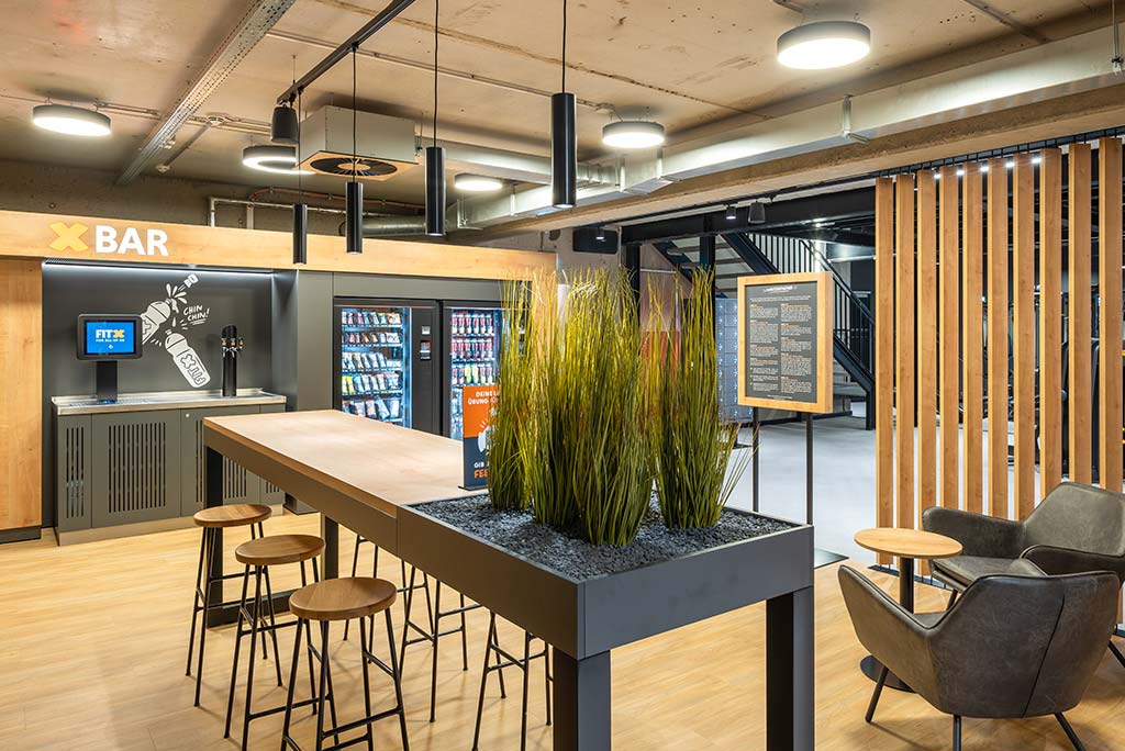 Abgetrennter Lounge-Bereich im FitX Fitnessstudio Düsseldorf-Derendorf mit verschiedenen Sitzmöglichkeiten. Der Bereich ist hell, freundlich und im industriellen Design gestaltet.