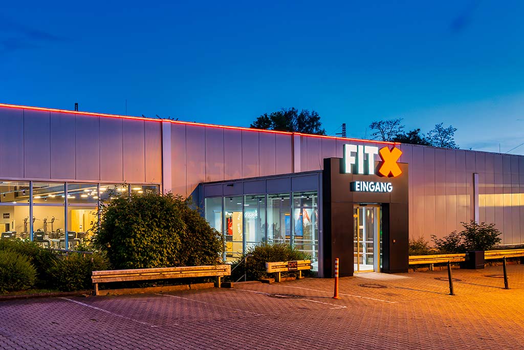 Außenansicht des FitX Fitnessstudios Dortmund-Phoenix See. Ein großes FitX-Logo mit orangefarbenem X ist zu sehen. Das Gebäude befindet sich in einem urbanen Umfeld.