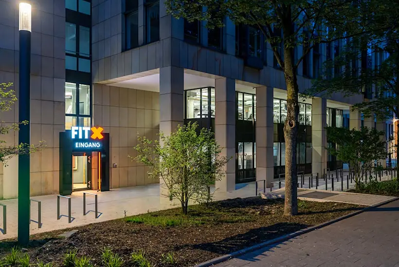 Bild: Außenansicht eines FitX Fitnessstudios. Ein großes FitX-Logo mit orangefarbenem X ist zu sehen. Das Gebäude befindet sich in einem urbanen Umfeld.