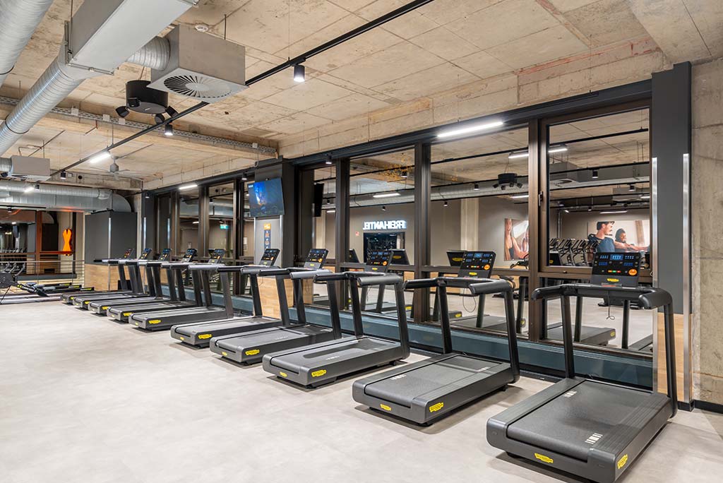 Offener Bereich für Ausdauertraining im FitX Fitnessstudio Essen-Bergerhausen mit verschiedenen Cardio-Geräten. An den Wänden hängen Fernseher.