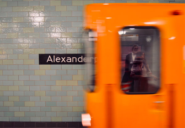 Bild: Eine U-Bahn fährt in die Station Alexanderplatz ein. Im Fenster spiegeln sich wartende Fahrgäste auf dem Bahnsteig.