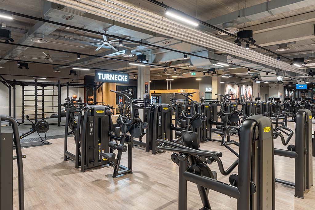 Gerätebereich im FitX Fitnessstudio Remscheid-Süd mit verschiedenen Kraftgeräten. Der Raum ist im industriellen Design gestaltet, mit offenen Deckenstrukturen und hellen Böden.