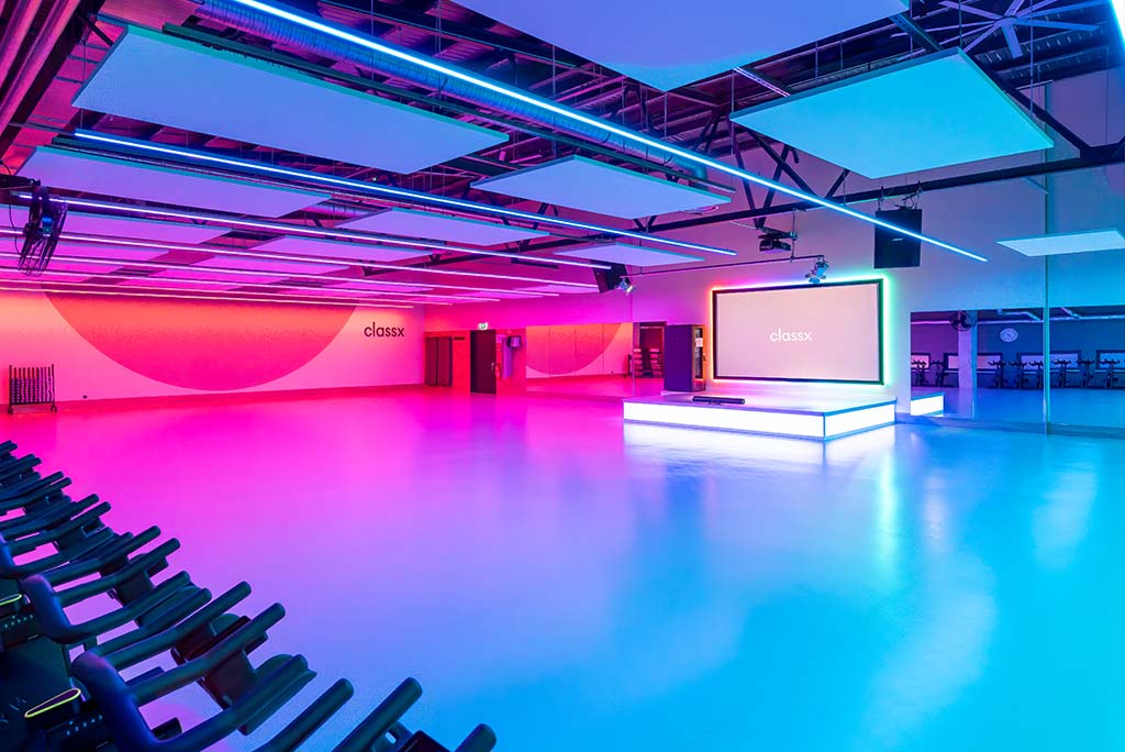 Großer, offener Kursraum im FitX Fitnessstudio Berlin-Ku'damm. An der hinteren Wand befindet sich eine erhöhte Bühne, dahinter eine Leinwand. Links und rechts davon sind Spiegelwände.