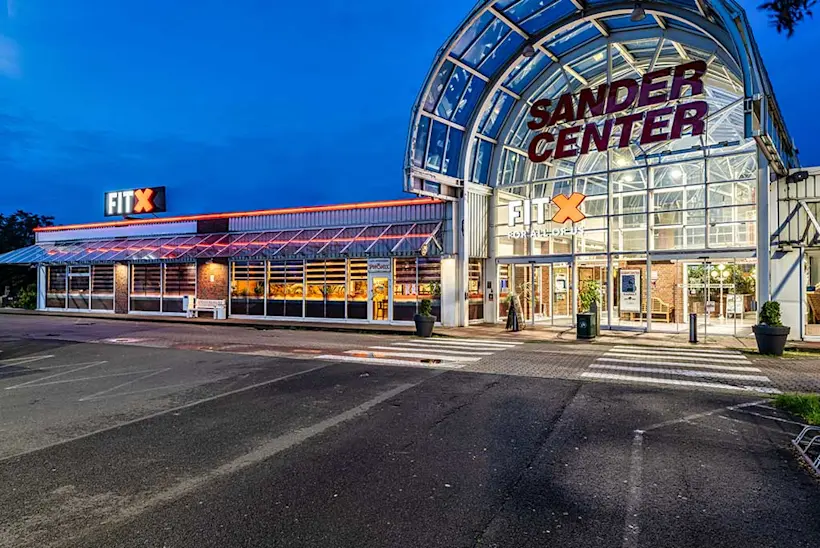 Bild: Außenansicht eines FitX Fitnessstudios. Ein großes FitX-Logo mit orangefarbenem X ist zu sehen. Das Gebäude befindet sich in einem urbanen Umfeld.