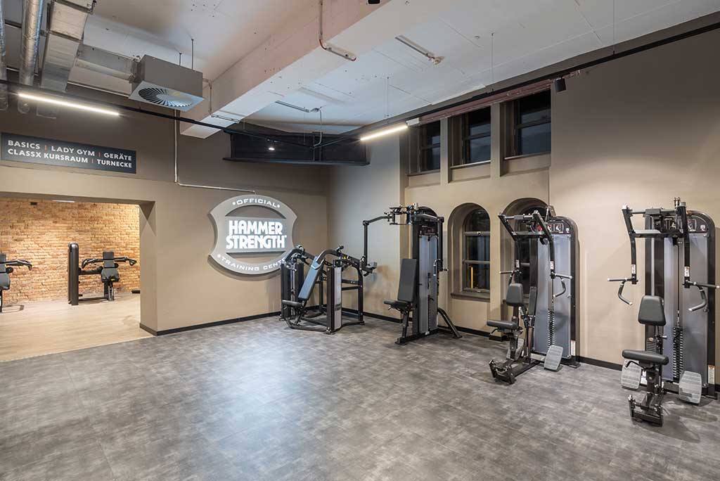 Zirkel-Bereich im FitX Fitnessstudio Berlin-Moabit, in dem verschiedene Trainingsgeräte kreisförmig angeordnet sind. Über den Geräten hängt ein großer Leuchtring, der in grün oder rot leuchtet und die Übungsdauer anzeigt.