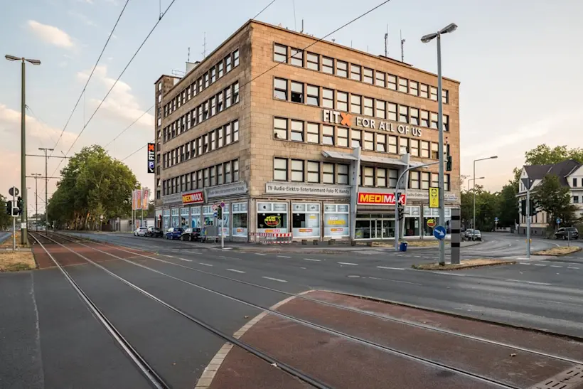 Bild: Außenansicht eines FitX Fitnessstudios. Ein großes FitX-Logo mit orangefarbenem X ist zu sehen. Das Gebäude befindet sich in einem urbanen Umfeld.