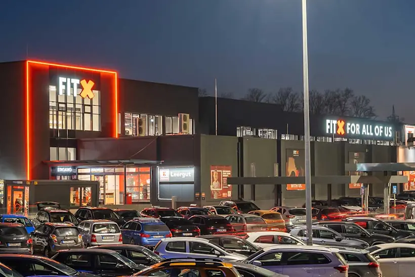 Bild: Außenansicht eines FitX Fitnessstudios. Ein großes FitX-Logo mit orangefarbenem X ist zu sehen. Das Gebäude befindet sich in einem urbanen Umfeld.