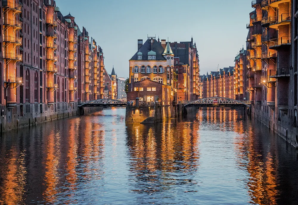 Bild: Blick vom Wasser der Elbe auf das Wasserschloss in der Speicherstadt bei Abenddämmerung.
