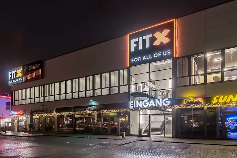 Bild: Außenansicht eines FitX Fitnessstudios. Ein großes FitX-Logo mit orangefarbenem X ist zu sehen. Das Gebäude befindet sich in einem urbanen Umfeld.