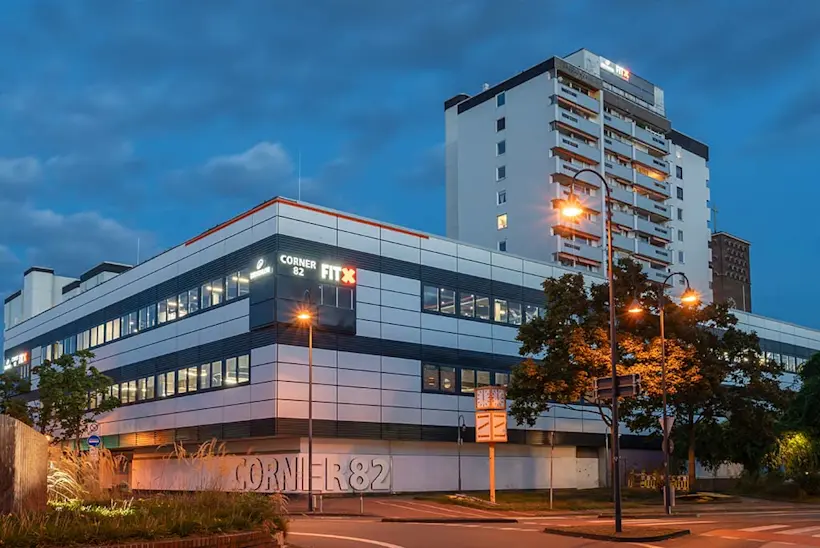 Bild: Außenansicht eines FitX Fitnessstudios. Ein großes FitX-Logo mit orangefarbenem X ist zu sehen. Das Gebäude befindet sich in einem urbanen Umfeld.