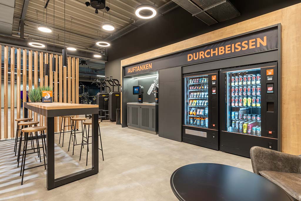 Abgetrennter Lounge-Bereich im FitX Fitnessstudio Dortmund-Phoenix See mit verschiedenen Sitzmöglichkeiten. Der Bereich ist hell, freundlich und im industriellen Design gestaltet.