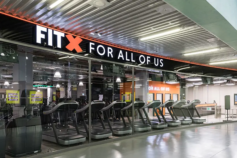 Bild: Außenansicht eines FitX Fitnessstudios. Ein großes FitX-Logo mit orangefarbenem X ist zu sehen. Das Gebäude befindet sich in einem urbanen Umfeld.